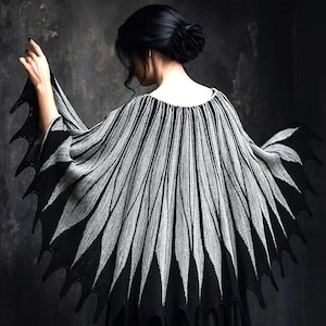 May include: A black and gray cape with a unique design. The cape features a series of vertical gray lines radiating from the neckline, with a black, jagged edge. The garment is worn over the shoulders, creating a dramatic silhouette.