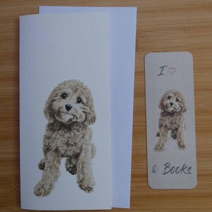 以下が含まれることがあります： ふわふわとした薄茶色の犬の精巧なイラストが描かれたグリーティングカードとブックマークのセット。カードには犬全体が描かれ、ブックマークには犬と「I ♡ & Books」の文字が描かれています。カードには白い封筒が添えられています。