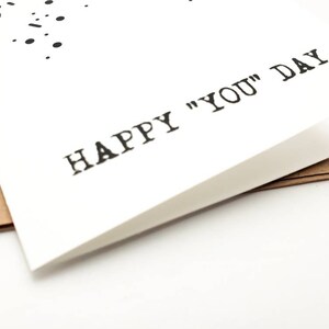 May include: A white card with black text that reads "Happy "You" Day".