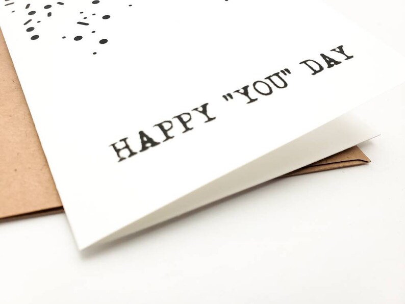 May include: A white card with black text that reads "Happy "You" Day".