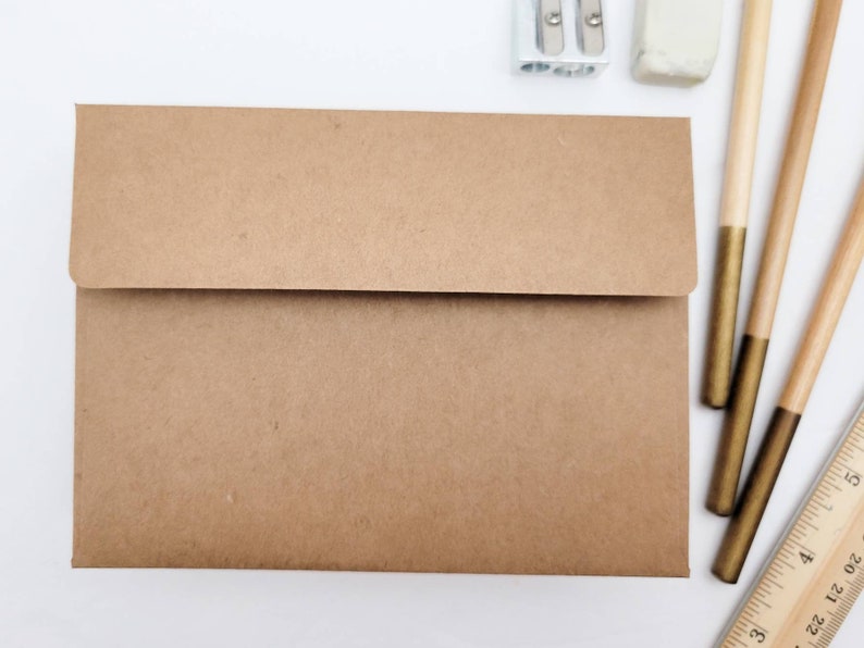 May include: A brown paper envelope with a flap on the top. The envelope is lying flat on a white surface.