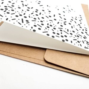 May include: A white card with a black and white geometric pattern is folded in half and placed on a brown envelope.
