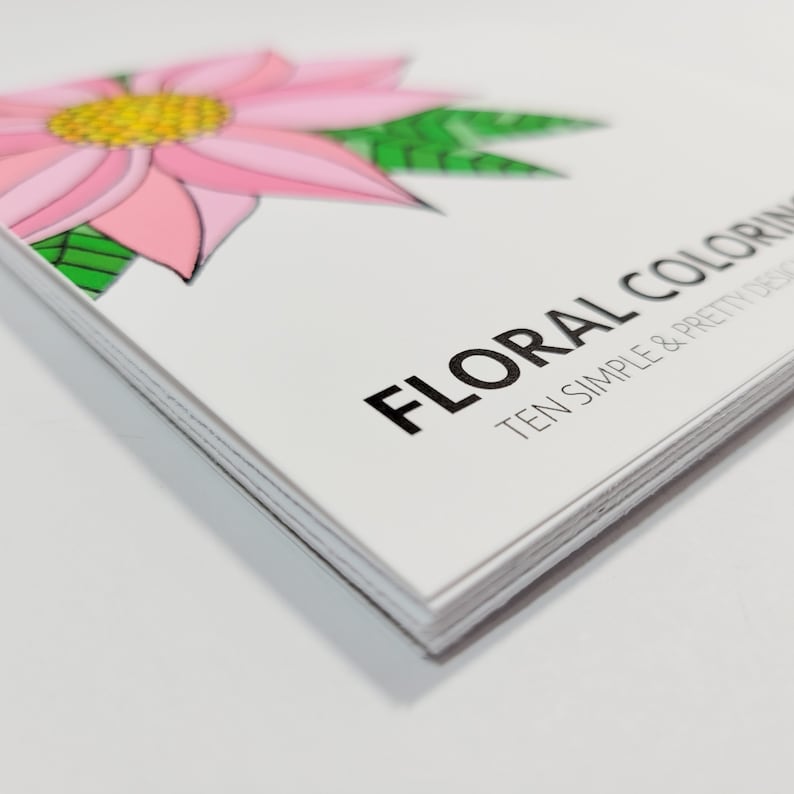 May include: A stack of colouring books with a pink flower and green leaves on the cover. The title of the book is "Floral Colouring: Ten Simple & Pretty Designs".