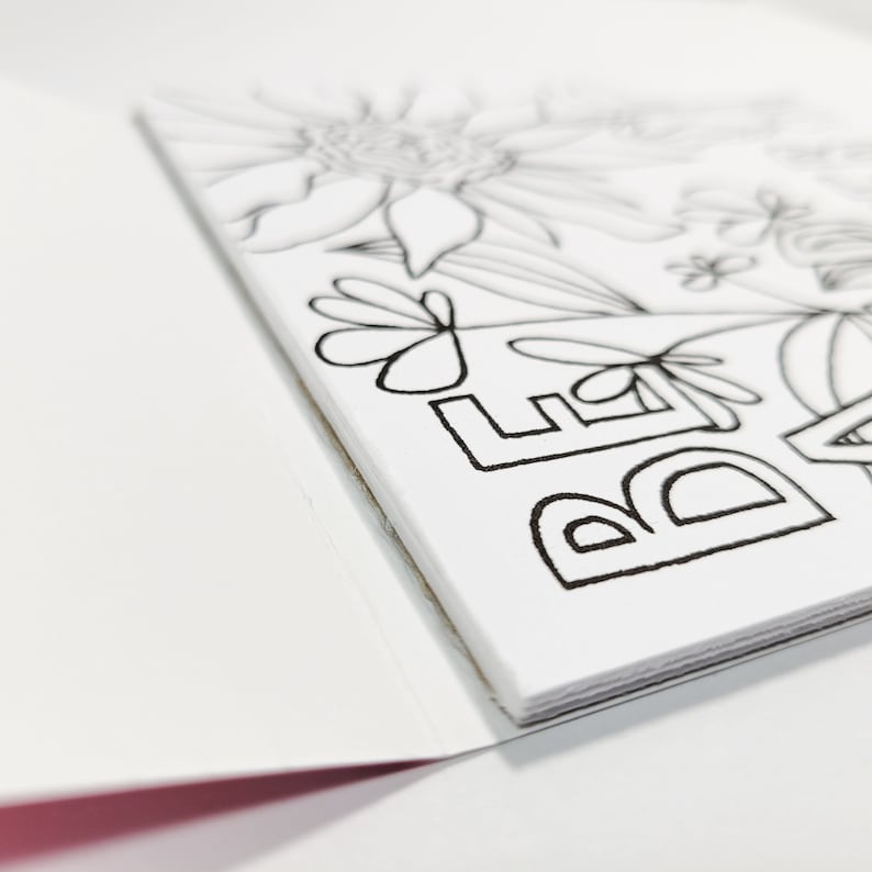 May include: A white card with black ink outlining the word "Believe" and floral designs. The card is folded in half.