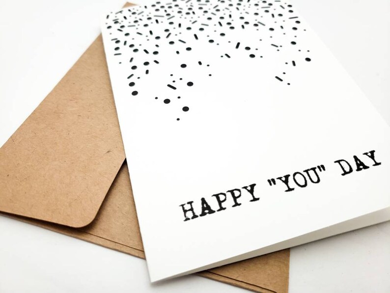 May include: A white card with a black confetti design and the text "HAPPY "YOU" DAY" printed in black.