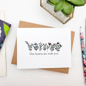 May include: A white card with a black line drawing of flowers and the text "Our hearts are with you."