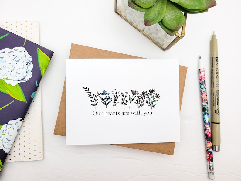 May include: A white card with a black line drawing of flowers and the text "Our hearts are with you."