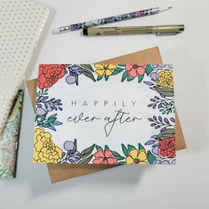 May include: A white card with a floral border and the text "Happily ever after" in black script.