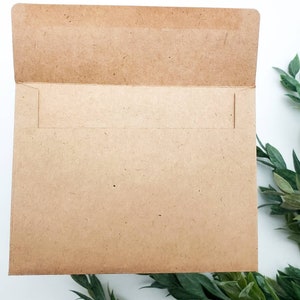 May include: A brown paper envelope with a white flap. The envelope is lying flat on a white surface.