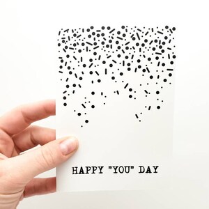 May include: A white card with black confetti and the text "HAPPY "YOU" DAY" printed on it.