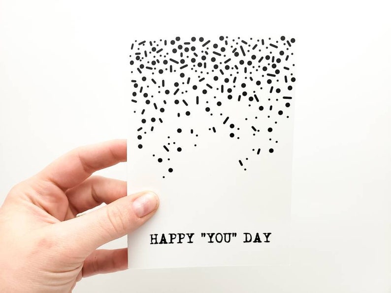 May include: A white card with black confetti and the text "HAPPY "YOU" DAY" printed on it.