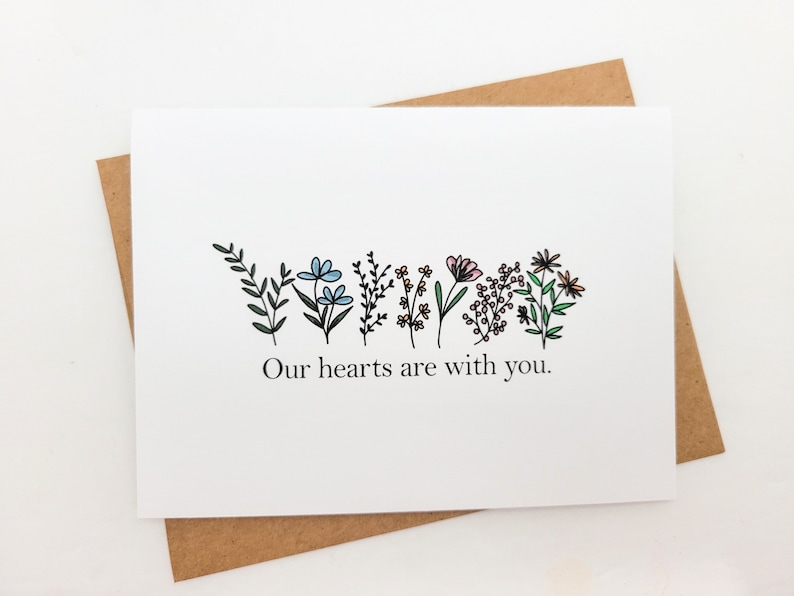 May include: A white card with a line of hand-drawn flowers in shades of blue, pink, and green. The text "Our hearts are with you." is printed below the flowers.