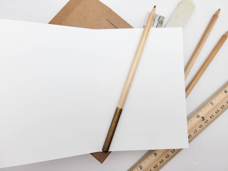 May include: A white sheet of paper with a brown pencil, a pencil sharpener, a ruler, and two wooden pencils on a white surface.