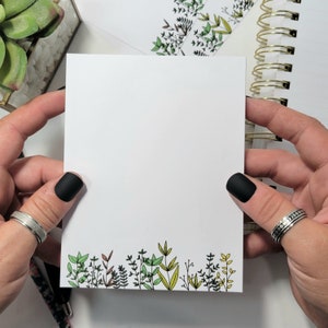 May include: A white notepad with a border of green, yellow, and brown leaves. The notepad is blank and ready to be written on.