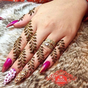 May include: A hand with henna designs on the fingers, featuring a leafy pattern. The nails are painted a bright pink and adorned with rhinestones and white flowers.