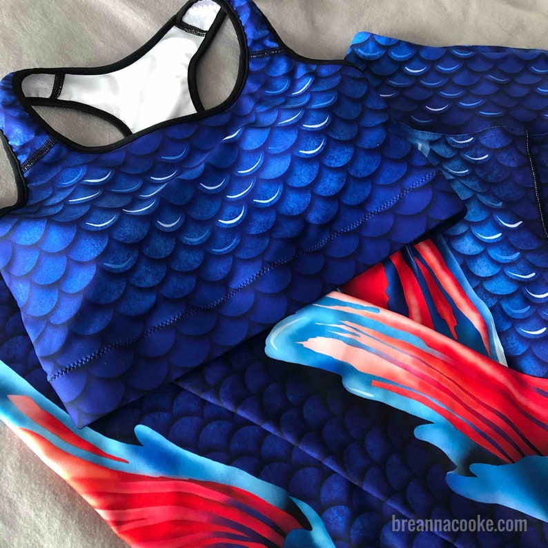 May include: A blue and red sports bra and leggings set with a mermaid scale pattern. The fabric has a shiny finish.