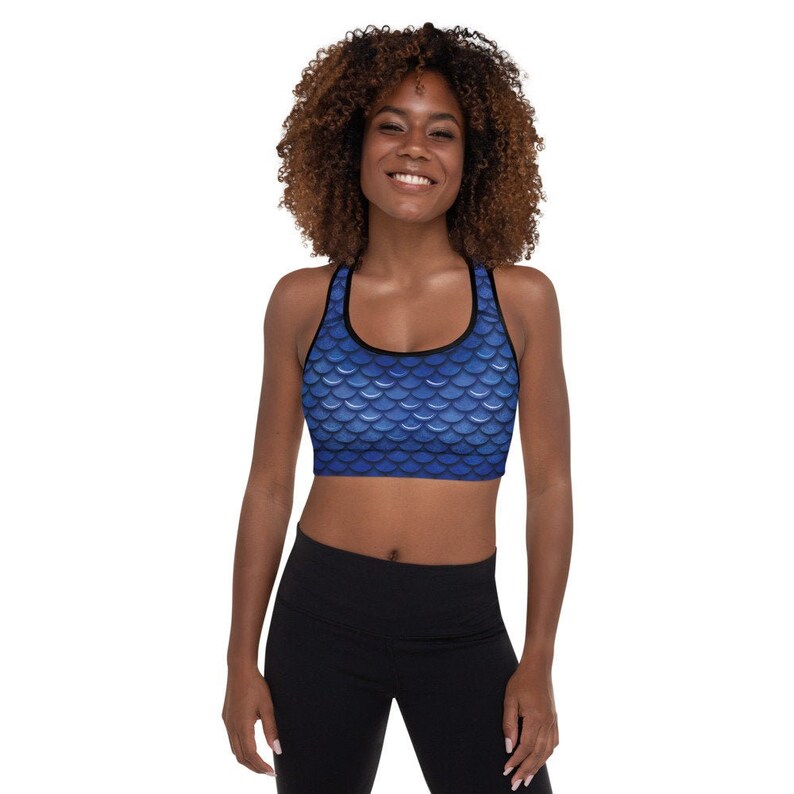 May include: A blue sports bra with a mermaid scale pattern. The bra has a black band around the top and bottom.