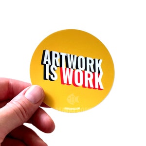 May include: A yellow round sticker with the text "ARTWORK IS WORK" in black, white, and red letters.