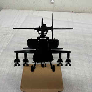 May include: A black metal silhouette of a helicopter with a rotating blade on top. The helicopter is sitting on a brown wooden base.