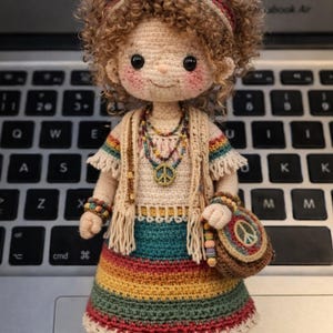 Puede incluir: Muñeca de ganchillo hecha a mano con temática hippie. La muñeca lleva un vestido arcoíris colorido, un chaleco con flecos y un collar con el símbolo de la paz. Tiene el pelo rizado castaño y una diadema a juego. La muñeca lleva un pequeño bolso con un símbolo de la paz.