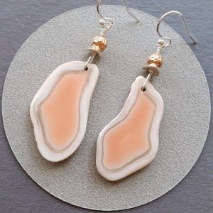 May include: A pair of dangle earrings featuring peach-colored agate slices with a white rim, accented with gold-toned beads and silver hooks.