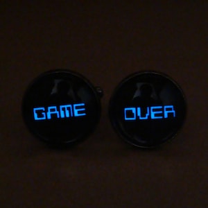 May include: A pair of black cufflinks with a blue glow. The left cufflink says "GAME" and the right cufflink says "OVER".