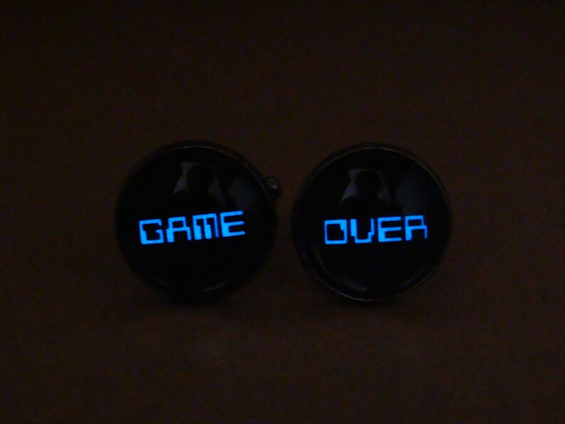 May include: A pair of black cufflinks with a blue glow. The left cufflink says "GAME" and the right cufflink says "OVER".