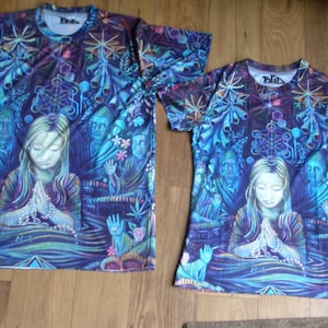 Może przedstawiać: Dwie koszulki z krótkim rękawem o żywym, psychodelicznym wzorze. Koszulki przedstawiają centralny obraz osoby ze złożonymi dłońmi w modlitwie, otoczonej postaciami i geometrycznymi wzorami w odcieniach niebieskiego, fioletowego i zielonego.