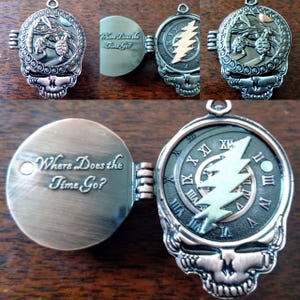 Könnte beinhalten: Bronzefarbener Anhänger in Schädelform mit Klappdeckel. Auf der einen Seite befindet sich ein Zifferblatt mit römischen Ziffern und einem Blitz. Auf der anderen Seite steht "Where Does the Time Go?" mit detaillierten Gravuren.