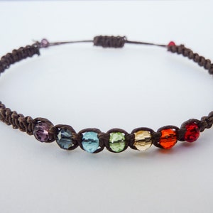 May include: A brown cord bracelet with seven colourful glass beads. The beads are purple, blue, light blue, green, yellow, orange and red.