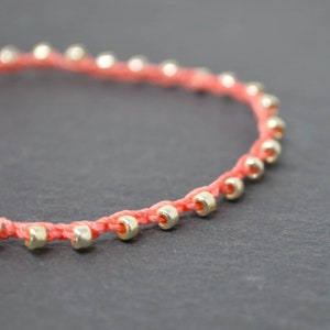 May include: A coral red string bracelet with small gold beads.
