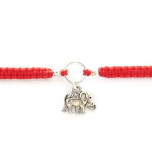 May include: Red string bracelet with a silver elephant charm. The charm is attached to a silver ring.