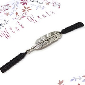 May include: Black cord bracelet with a silver feather charm. The bracelet is on a white card with the text "Wish Knots" in pink.