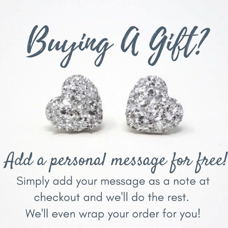 May include: Two silver heart-shaped stud earrings with a glittery texture. The image includes the text "Buying a Gift?" and "Add a personal message for free!"