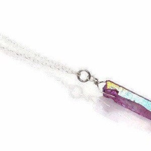 May include: A silver chain necklace with a pendant featuring a purple, iridescent crystal. The crystal has a rectangular shape with a metallic sheen, displaying hues of purple, gold, and blue. The necklace is set against a white background.