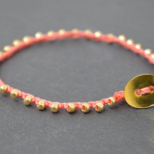 May include: A coral red braided bracelet with gold beads and a gold button closure.