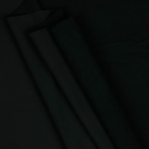 May include: A close-up shot of black fabric, with visible folds and shadows. The fabric appears to be a solid color, with a matte finish. The folds create a sense of depth and texture, suggesting a soft or drapable material.