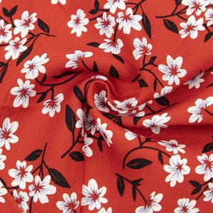 May include: A vibrant red fabric featuring a repeating pattern of white five-petaled flowers with small dark red centers. The floral design includes thin black stems and small black leaves scattered throughout the textile, creating a dense botanical print.