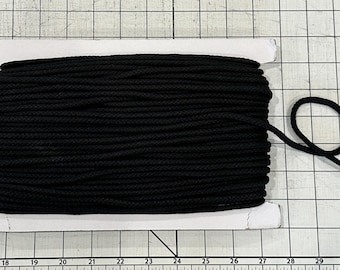 May include: A spool of black rope, tightly wound and ready for use. The rope is a solid black color, and a loop is formed at the end of the rope. The spool is on a white cardboard base.