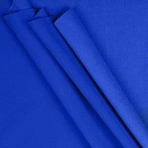 May include: A close-up of several folds of vibrant blue fabric. The fabric has a smooth texture and appears to be a medium-weight material. The folds create shadows and highlights, adding depth to the image. The color is a rich, saturated blue.