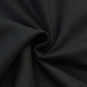 May include: Close-up of a black fabric with a soft, fuzzy texture. The fabric is folded and draped, showing its smooth surface and subtle wrinkles.