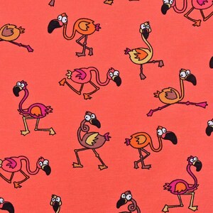 May include: A vibrant coral-colored fabric featuring a repeating pattern of cartoon flamingos in various poses. The flamingos are illustrated in shades of pink and orange with black beaks and wide, expressive eyes, scattered across the surface.