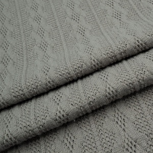 May include: Gray knitted fabric with a textured, diamond-shaped pattern. The fabric is folded in thirds, showing the texture from different angles.