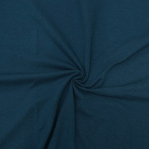 May include: A close-up of a teal blue fabric with a soft, textured surface. The fabric is folded and draped, showing its smooth texture.