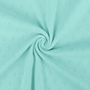 May include: A close-up shot of a soft, mint-green fabric with a diamond-shaped pattern. The fabric is tightly woven and has a slight sheen, with a spiral in the center. The texture appears to be knit or crocheted, suitable for clothing or home decor.