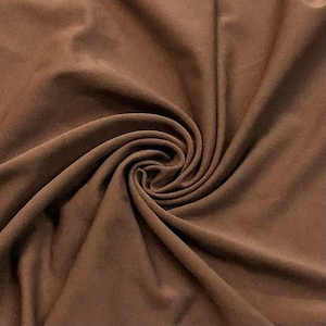 May include: A close-up of a brown fabric with a soft, smooth texture. The fabric is folded and draped, creating a sense of movement and flow.