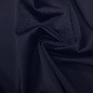 May include: A close-up of a dark blue fabric with a smooth, slightly textured surface. The fabric is folded and draped, showing its soft and flowing nature.