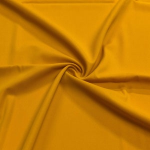 May include: A close-up of a smooth, bright yellow fabric. The fabric is folded and draped, showing its texture and colour.
