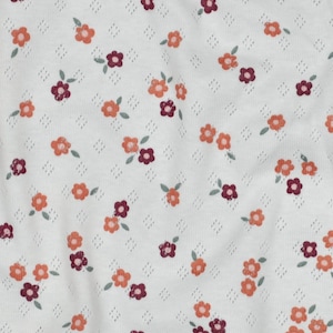 May include: A white fabric featuring a repeating pattern of small orange and dark maroon flowers with tiny green leaves. The material has a subtle, textured diamond-shaped eyelet pattern woven throughout the white background.