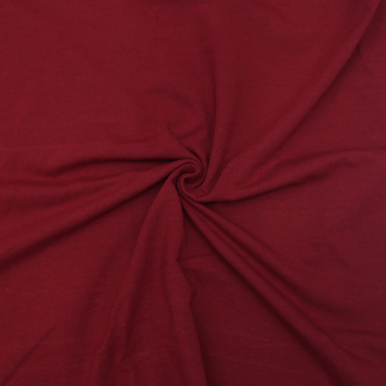 May include: A close-up of a deep red fabric with a soft, smooth texture. The fabric is folded and draped, creating a sense of movement and flow.